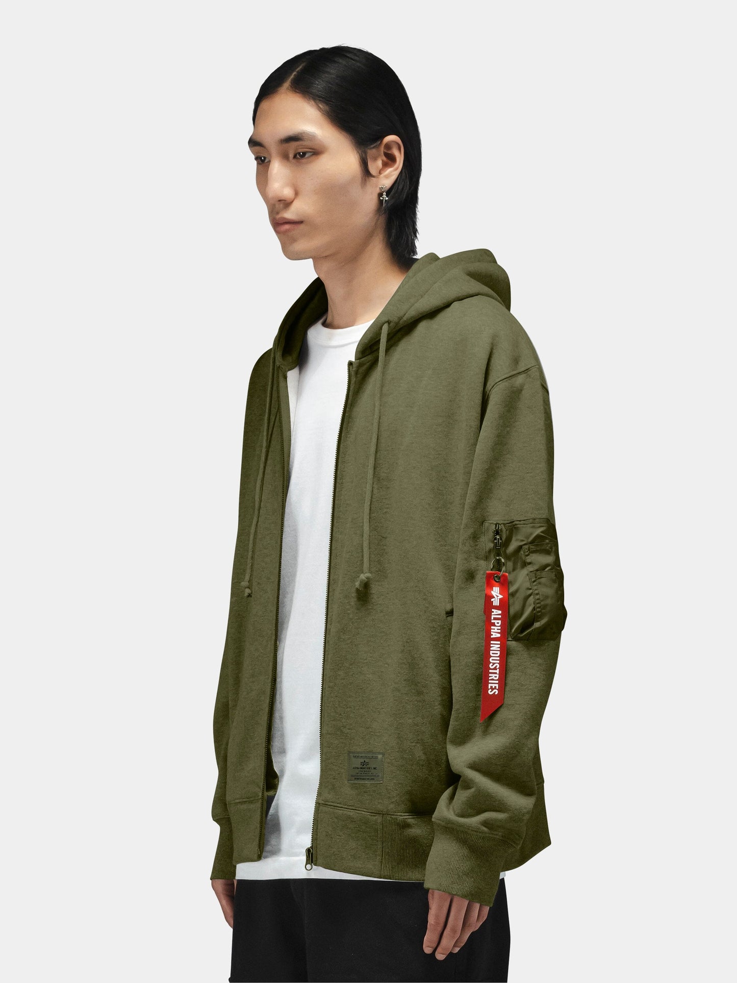 Alpha Industries Utility Pocket Full Zip Up, olive green hoodie with red Remove Before Flight sleeve tag, white t-shirt underneath.