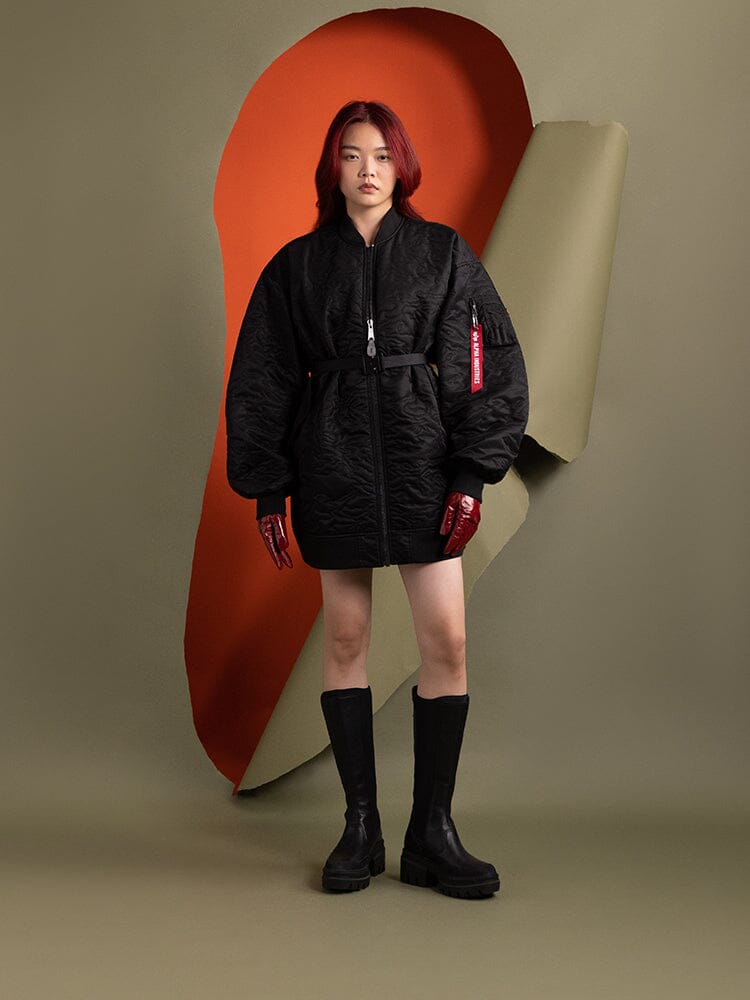 A person wearing the Women's Camo Quilted Belted MA-1 Bomber Jacket in black by Alpha Industries and boots stands.