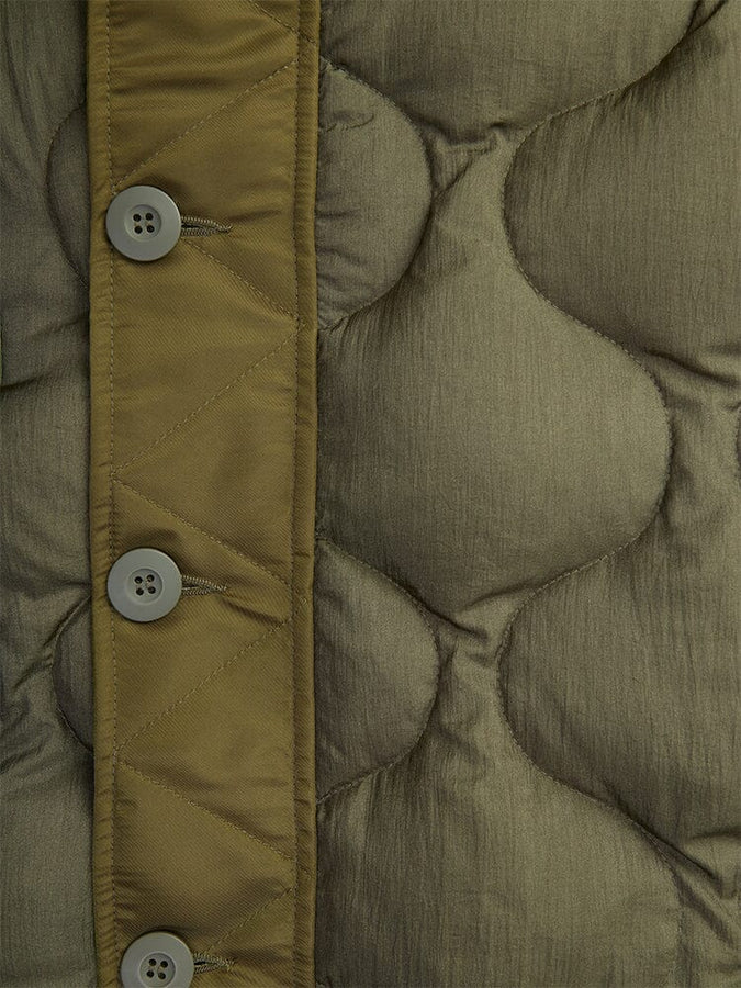 A close-up of the olive green quilted fabric from the Women's M-65 Fishtail Puffer by Alpha Industries features a row of four buttons on the left. The texture showcases curved stitching and onion quilting near the buttons.
