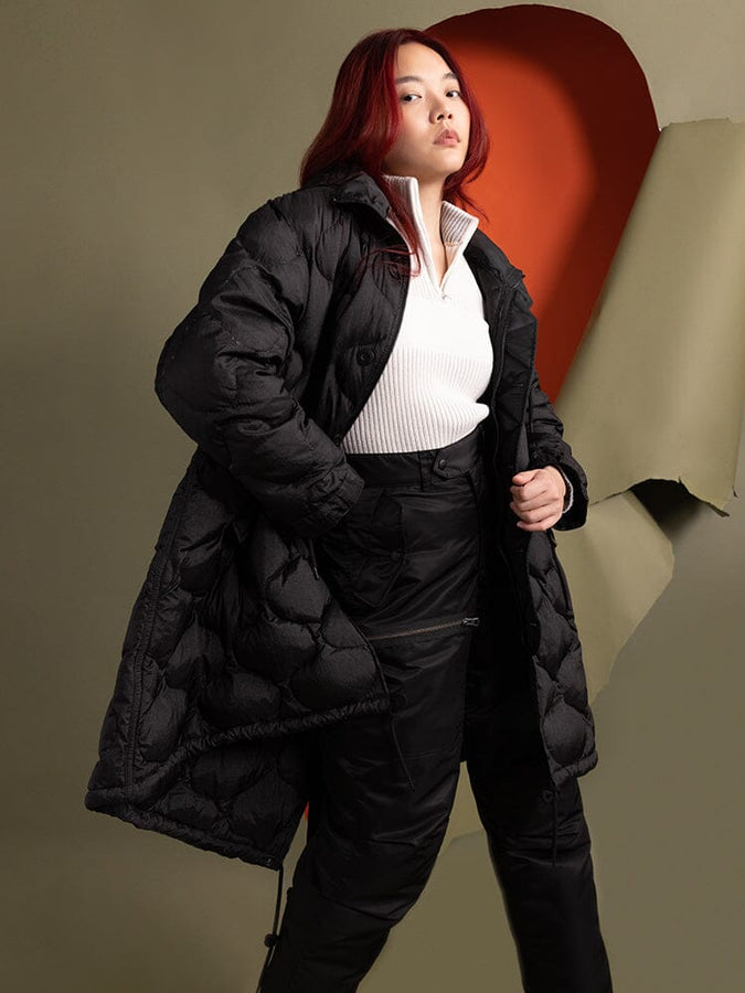 A person standing to the side wearing the Women's M-65 Fishtail Puffer in black from Alpha Industries.
