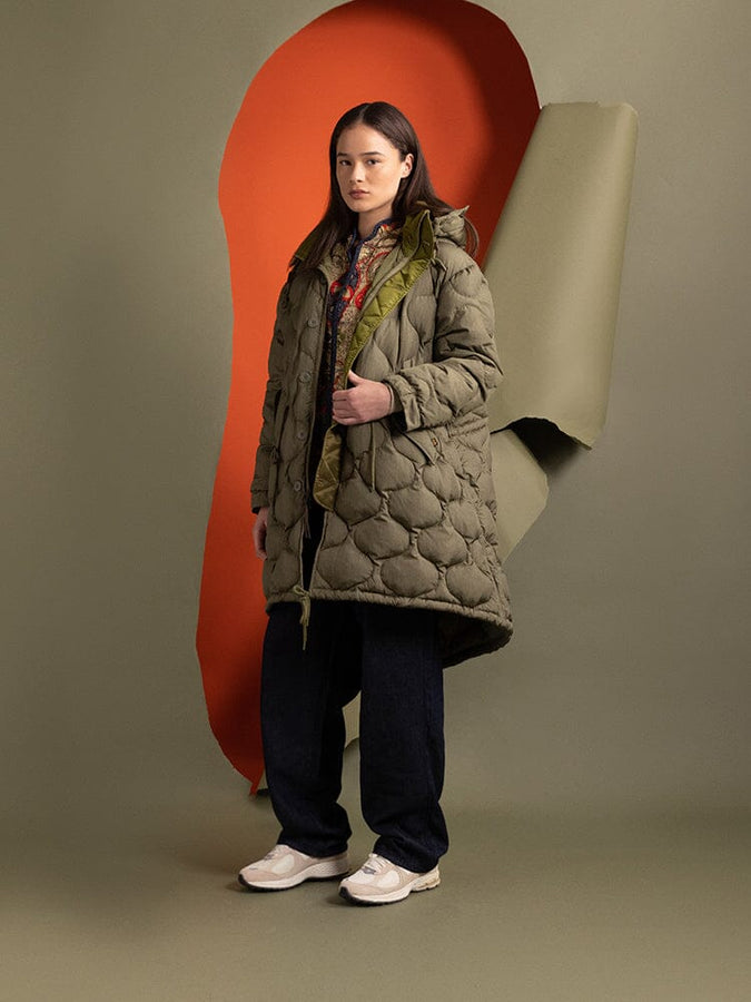 A person wearing the Women's M-65 Fishtail Puffer in green from Alpha Industries, characterized by onion quilting in an olive-green shade, paired with dark pants.