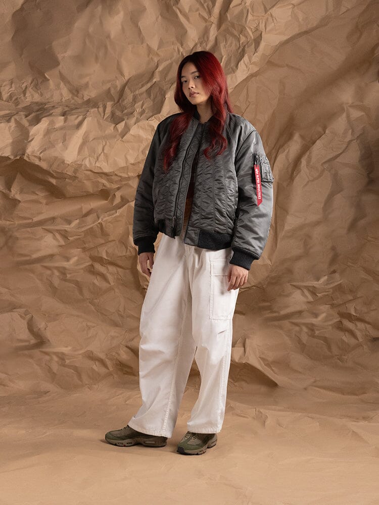 An person standing to the side wearing the Women's MA-1 Shirring Bomber Jacket in field gray from Alpha Industries