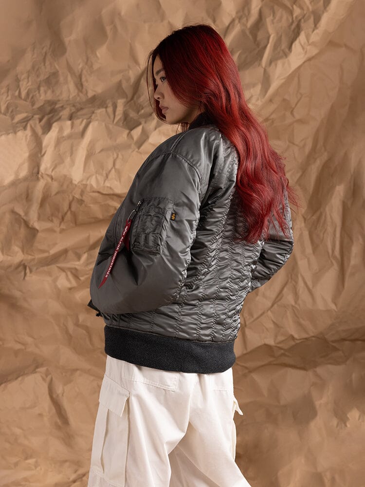 A person stands sideways, showcasing the Women's MA-1 Shirring Bomber Jacket in field gray by Alpha Industries.
