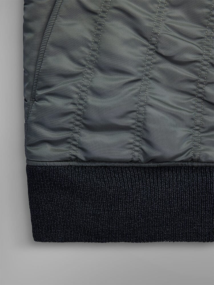 Close-up of the fabric from the Women's MA-1 Shirring Bomber Jacket by Alpha Industries, featuring quilted field gray material with vertical stitching and a textured black hem.