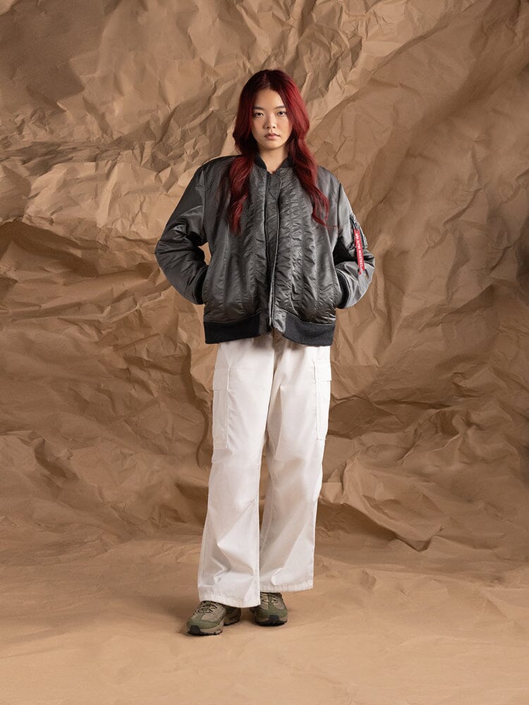 A person wearing the Women's MA-1 Shirring Bomber Jacket in field gray by Alpha Industries, paired with white pants.