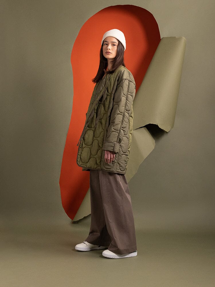 Side-view of a person wearing the Women's Mixed Media Quilted Long Liner in OG-107 Green by Alpha Industries.