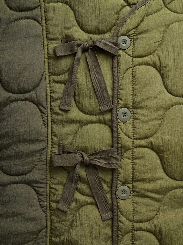 Close-up view of the Women's Mixed Media Quilted Long Liner in OG-107 Green by Alpha Industries displays wave-patterned onion quilting, two tied bows, and a row of four buttons on the right side.