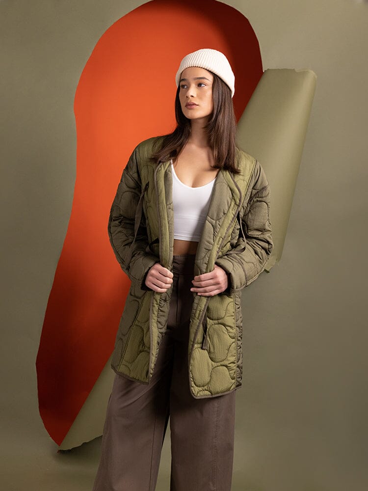 A woman in an Alpha Industries Women's Mixed Media Quilted Long Liner in OG-107 Green stylishly layers with a white top.