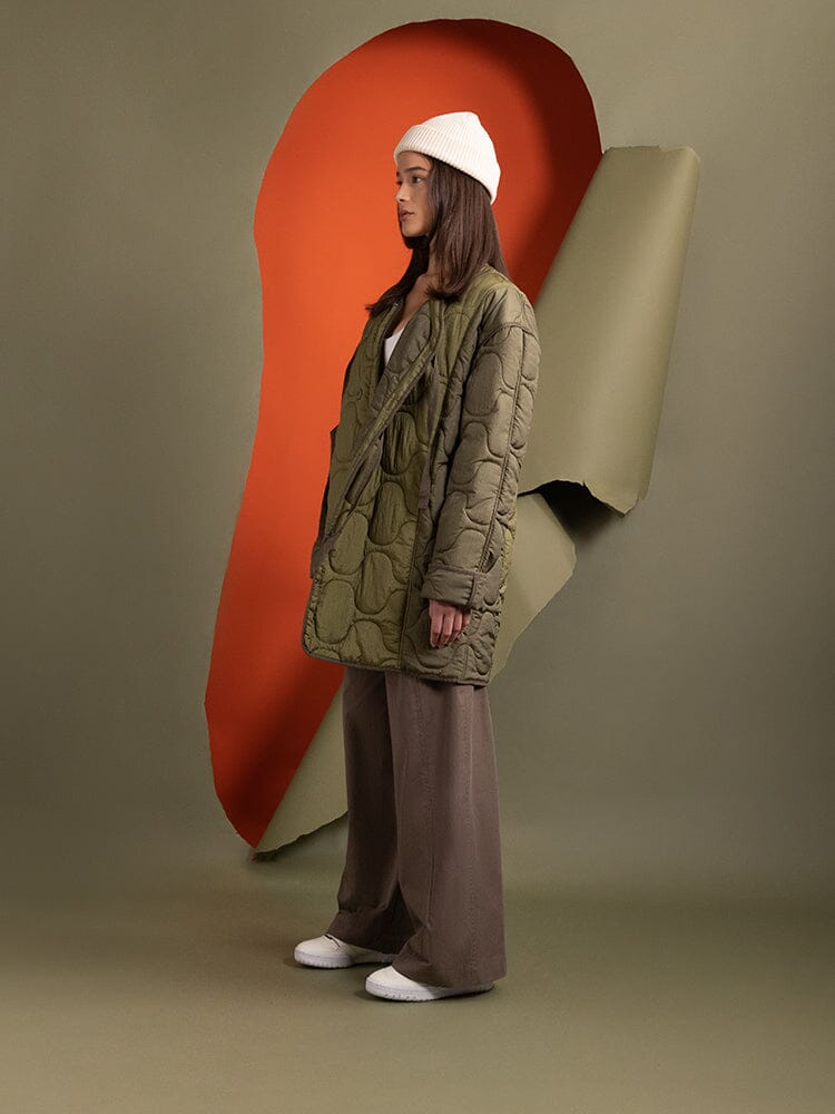 Side-view of a person wearing the Women's Mixed Media Quilted Long Liner in olive green by Alpha Industries.