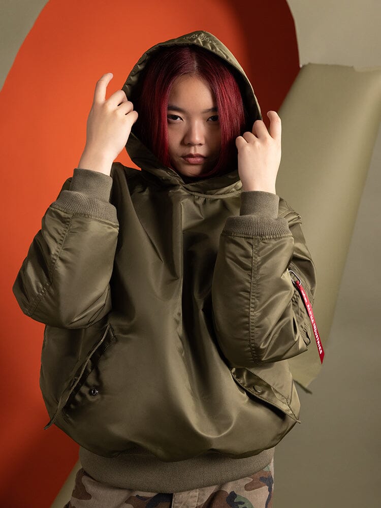 A person wearing the Women's Pull-Over MA-1 Jacket Hoodie in OG-107 Green by Alpha Industries.