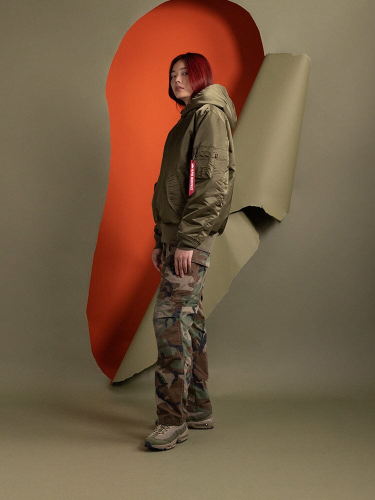Side view of a person wearing the Women's Pull-Over MA-1 Jacket Hoodie  in OG-107 Green by Alpha Industries.