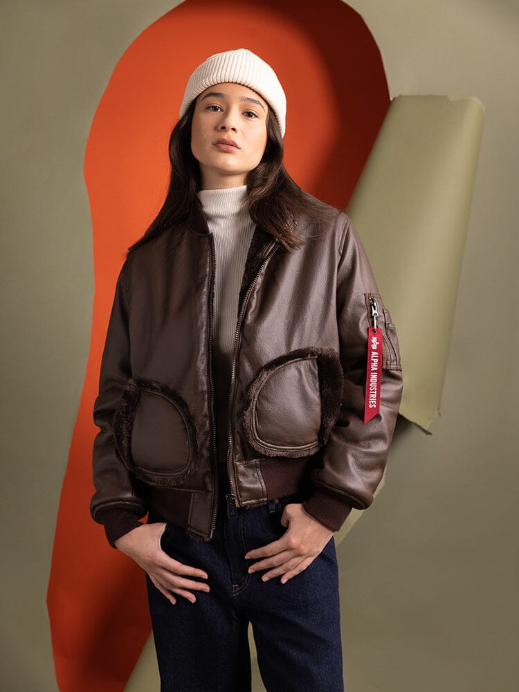 A person wearing the Women's Reversible Faux Leather MA-1 Bomber Jacket in brown chocolate by Alpha Industries.