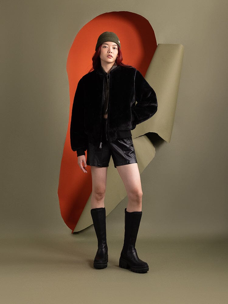A person wearing the reversible side of the Women's Reversible Faux Leather MA-1 Bomber Jacket in black by Alpha Industries.