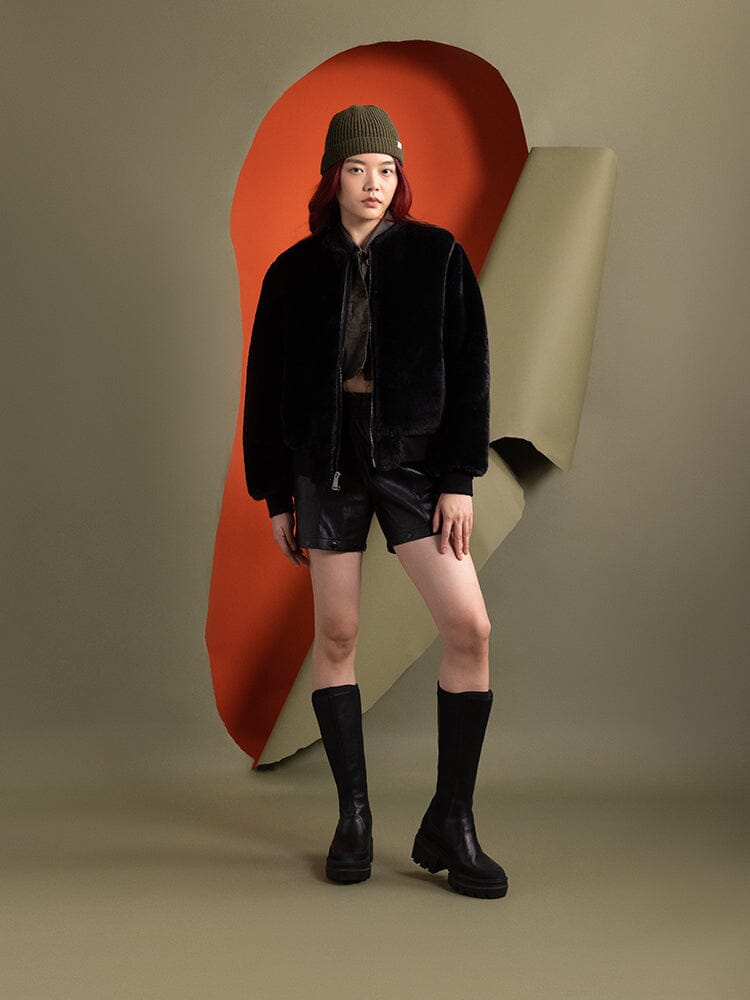 A person wearing the reversible side of the Women's Reversible Faux Leather MA-1 Bomber Jacket in black by Alpha Industries.