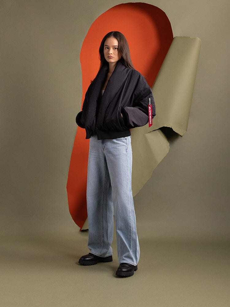 Full body view of a person standing to the side wearing the Women's Shawl Collar Bomber Jacket in black by Alpha Industries.