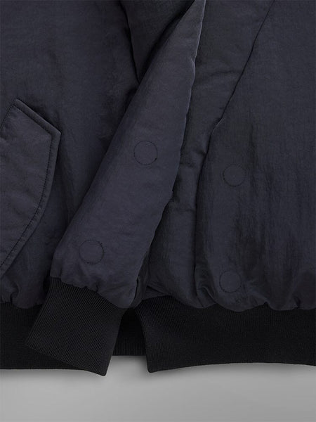 Close-up of the Women's Shawl Collar Bomber Jacket in a dark shade, showcasing its padded design with visible stitching and pocket detail. The sleeves and hem are accented with black ribbed cuffs.