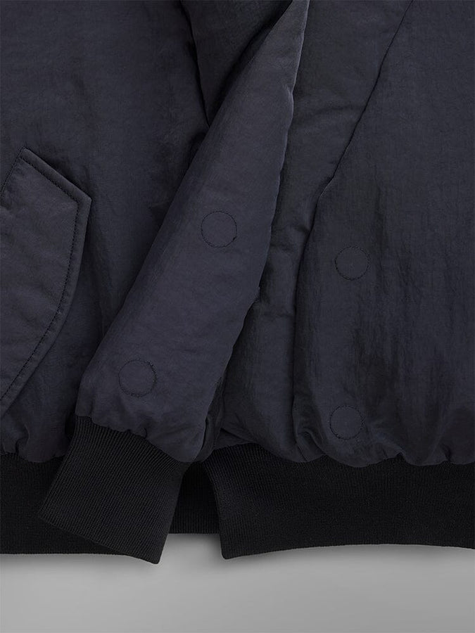 Close-up of the Women's Shawl Collar Bomber Jacket in a dark shade, showcasing its padded design with visible stitching and pocket detail. The sleeves and hem are accented with black ribbed cuffs.