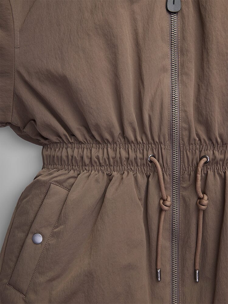 A detailed look at the Women's Short Cinched Waist Jacket by Alpha Industries, showcasing a front zipper, adjustable drawcord waist for a customized fit, and a buttoned pocket, all enhanced by a warm quilted lining.