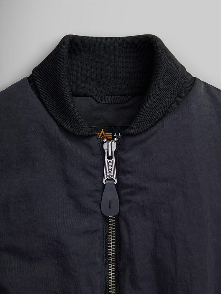 Close-up of the Women's Short Cinched Waist Jacket by Alpha Industries, showcasing its black design with a zipper closure and ribbed collar. The jacket features a quilted lining for added warmth.