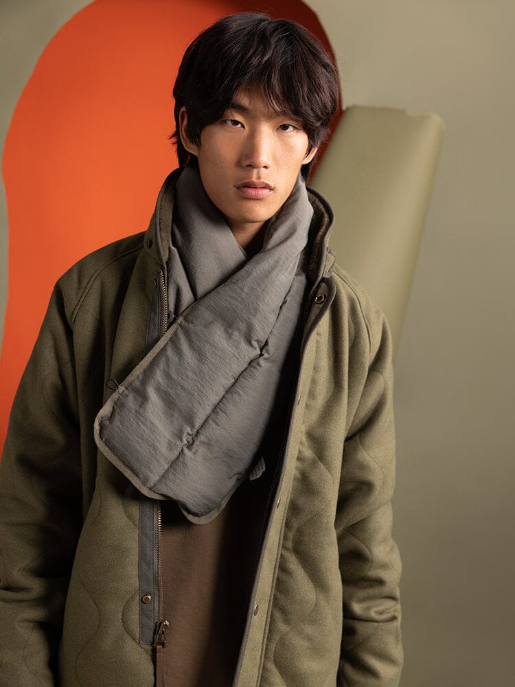 A person wearing an Alpha Industries Wool Deck Jacket in green, featuring a quilted design with faux down fill, and paired with a gray scarf.