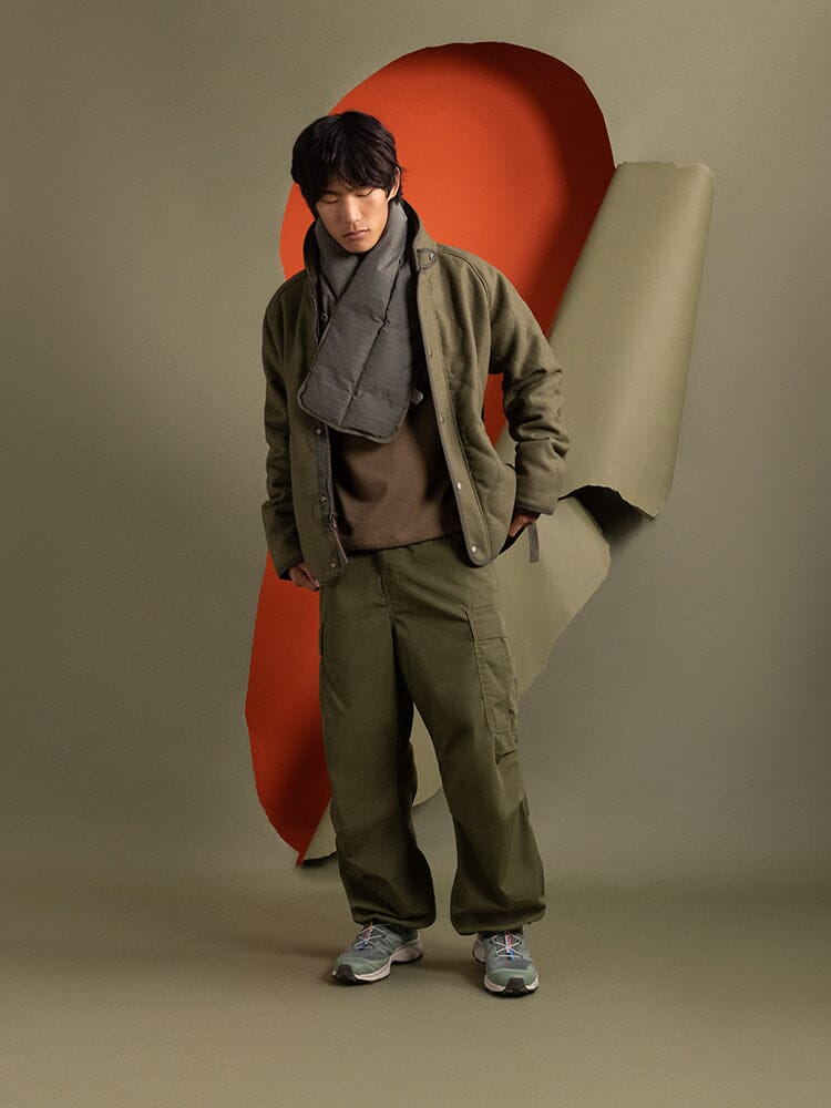 An individual wearing the Alpha Industries Wool Deck Jacket in green and matching pants, accessorized with a gray scarf.