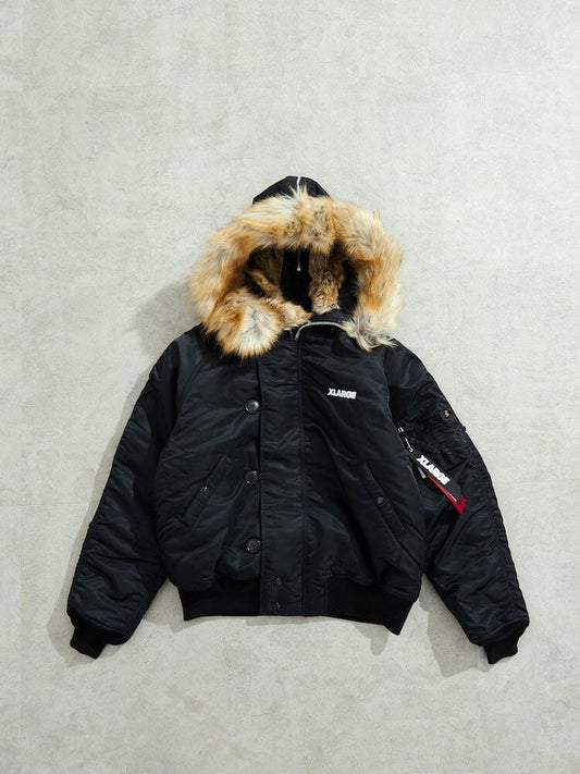 N-2B Core Spec Parka by Alpha Industries in black with water-repellent nylon shell, synthetic fur-lined hood, front buttons, arm zip pocket, and white chest logo.