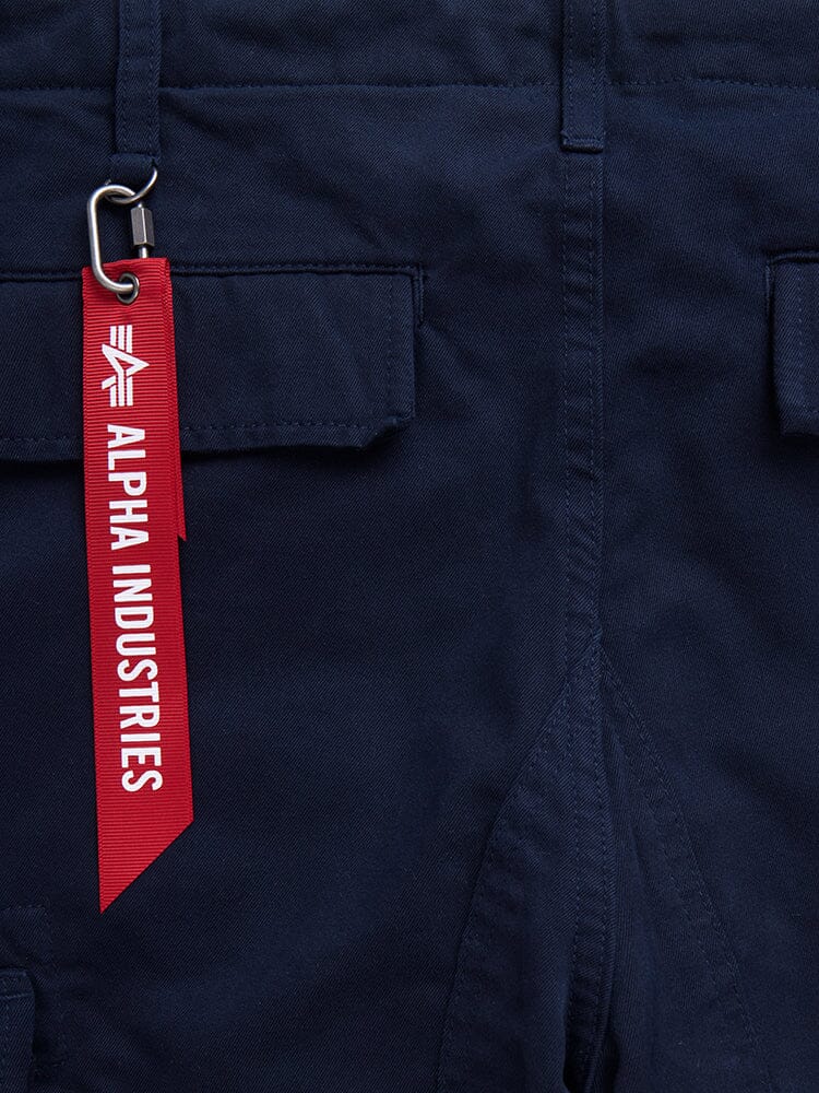Alpha Industries Acu Pant in navy with utility flap pockets and red tag on metal clip.