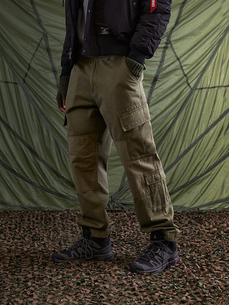 Alpha Industries Acu Pant in olive with utility pockets, paired with a black jacket and dark hiking shoes.