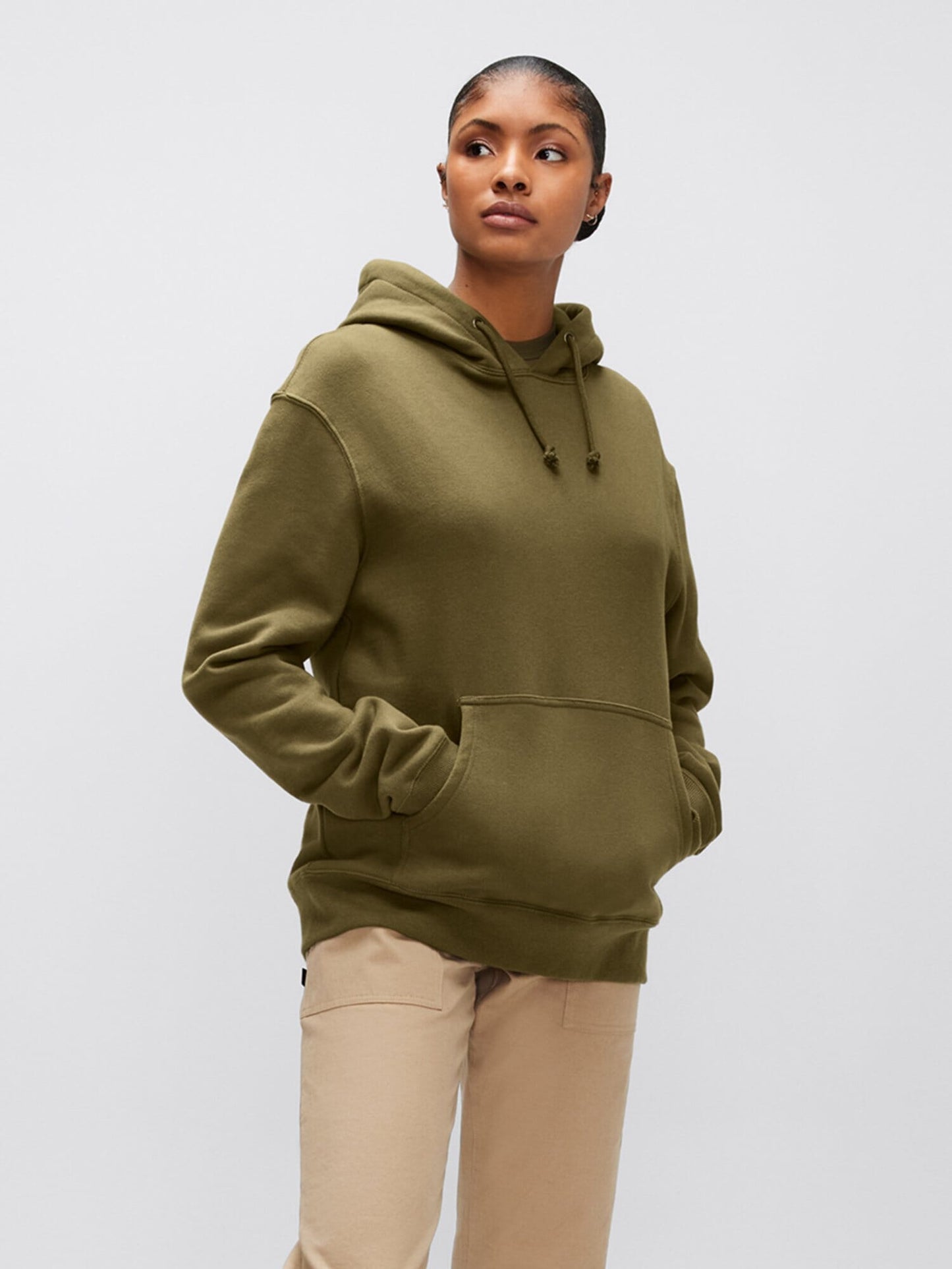 An individual wearing an Alpha Industries, Inc. Alpha Hoodie in unisex olive green, complete with an Alpha applique, and paired with beige pants to highlight the comfort of cotton fabric.
