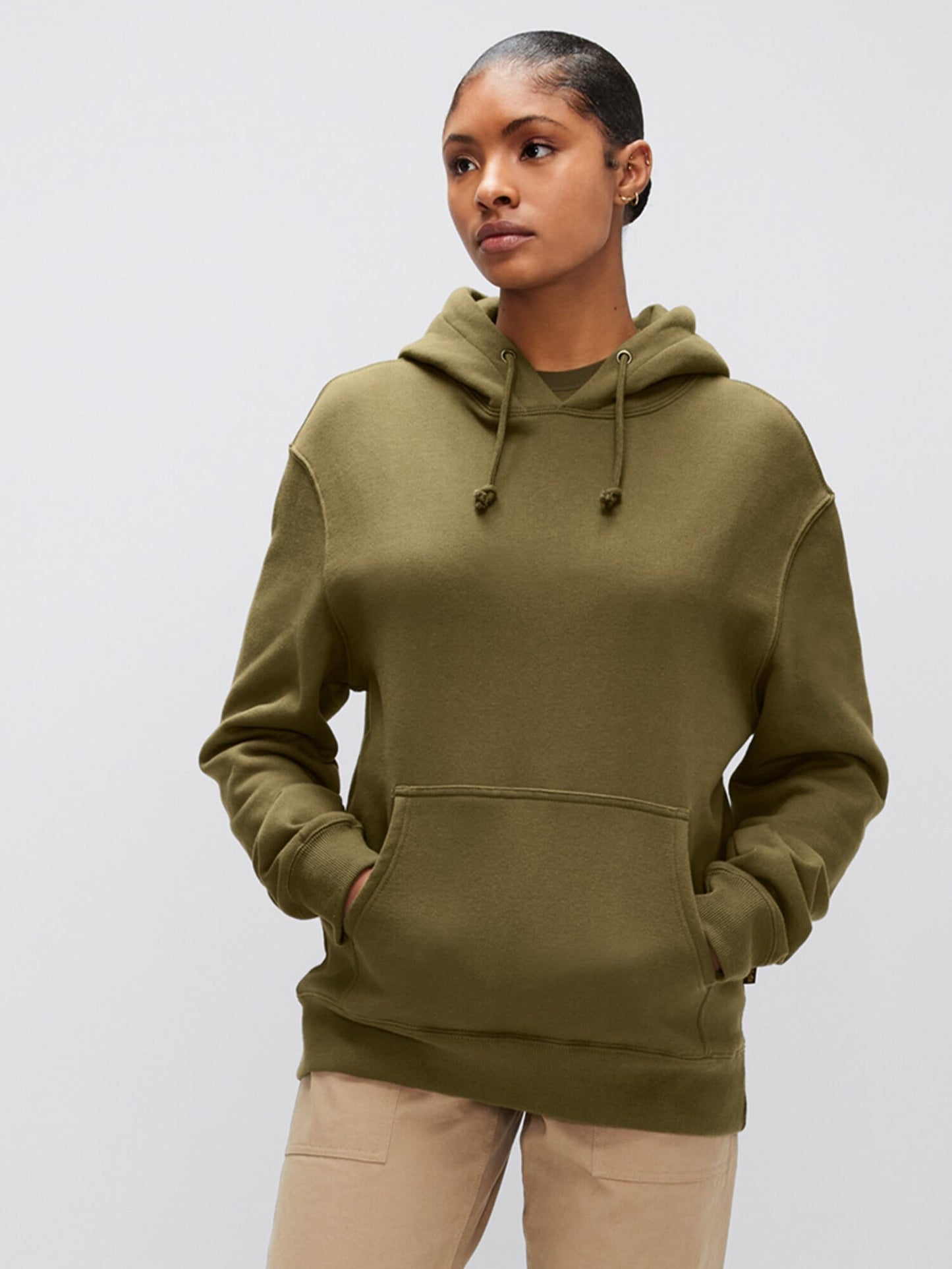A person wearing the Alpha Hoodie from Alpha Industries, Inc., crafted from soft cotton fabric, stands with hands in the front pocket, gazing slightly off to the side.