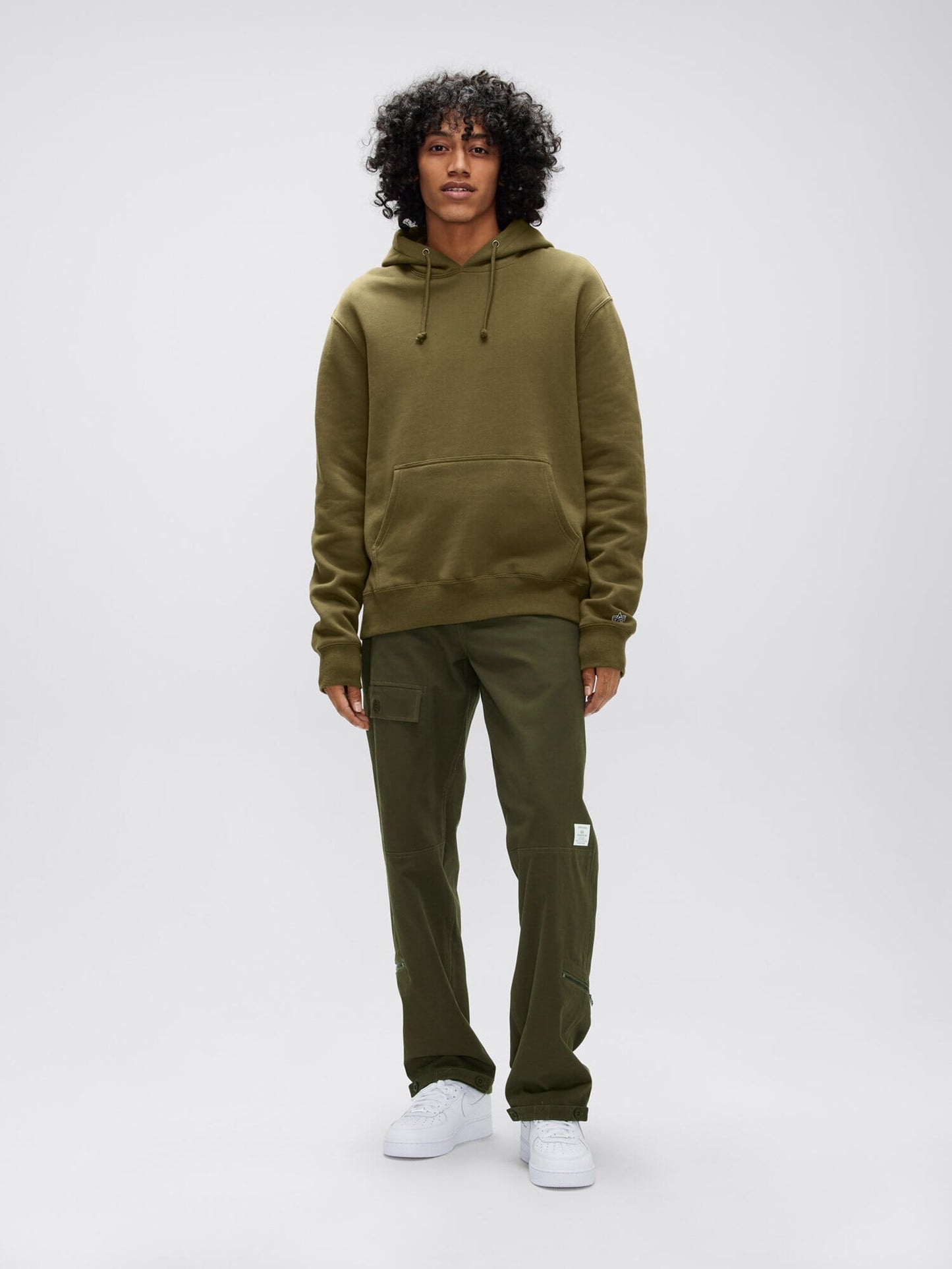 A person dressed in an olive green Alpha Hoodie by Alpha Industries, Inc., coupled with cargo pants and white sneakers.