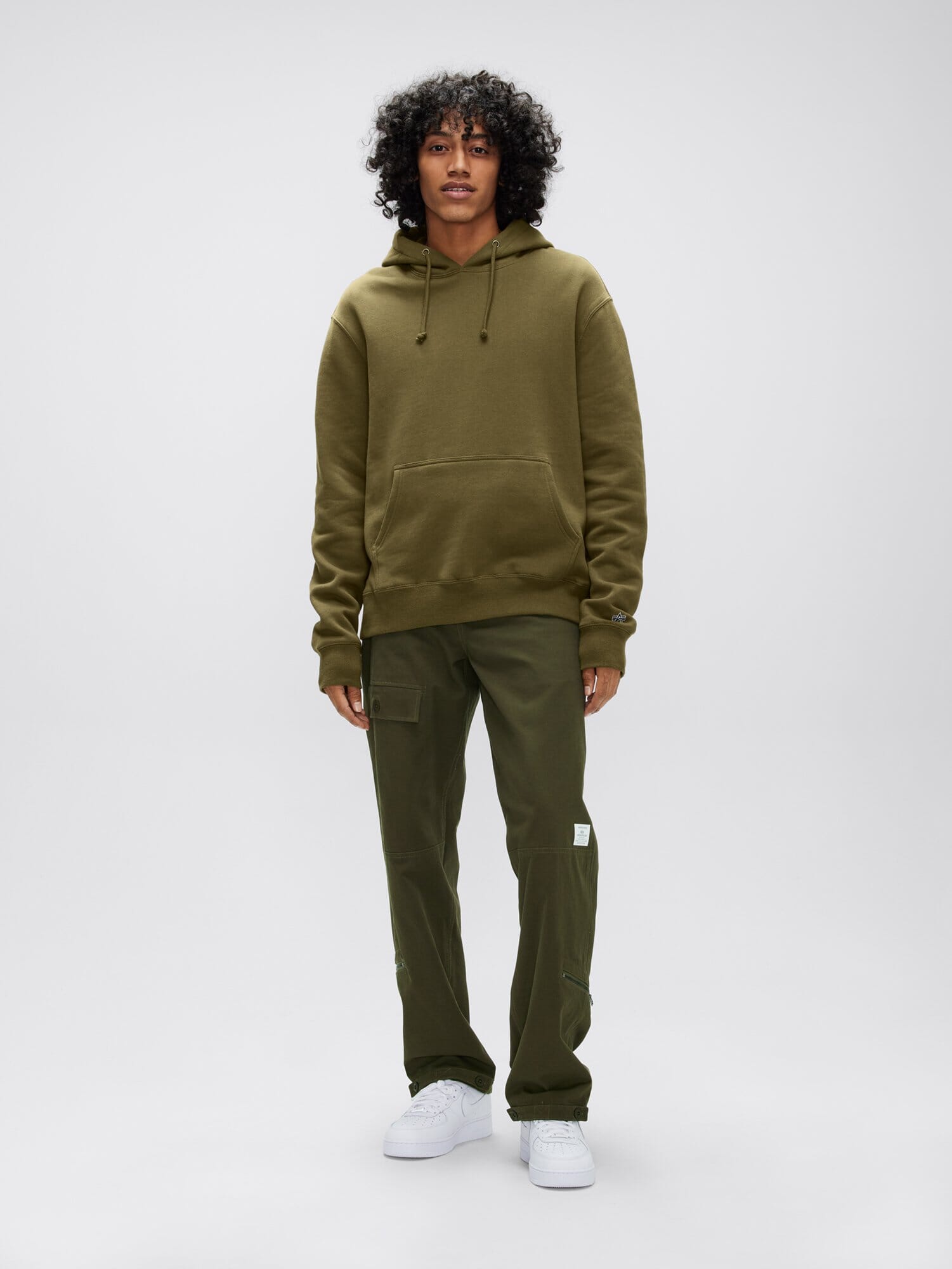 A person dressed in an olive green Alpha Hoodie by Alpha Industries, Inc., coupled with cargo pants and white sneakers.