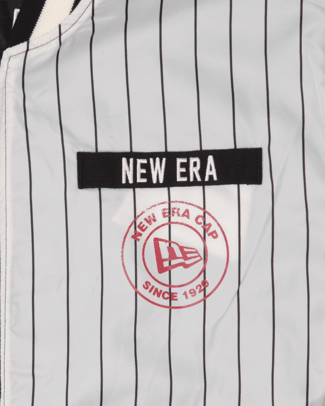 Close-up of the Alpha X New Era L-2B Bomber Jacket by Alpha Industries, featuring a striped ripstop design, a New Era patch, and a circular logo with "New Era Cap Since 1920" and a flag emblem. It combines classic style with modern durability.