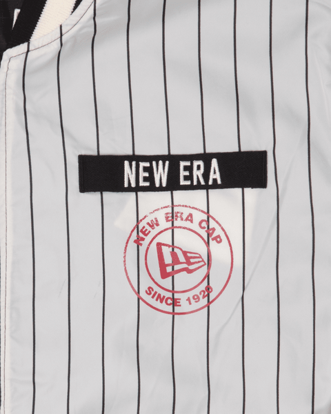 Close-up of the Alpha X New Era L-2B Bomber Jacket by Alpha Industries, featuring a striped ripstop design, a New Era patch, and a circular logo with "New Era Cap Since 1920" and a flag emblem. It combines classic style with modern durability.