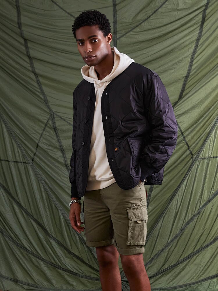 Alpha Industries Als/92 Liner in black, white hoodie, olive green cargo shorts.