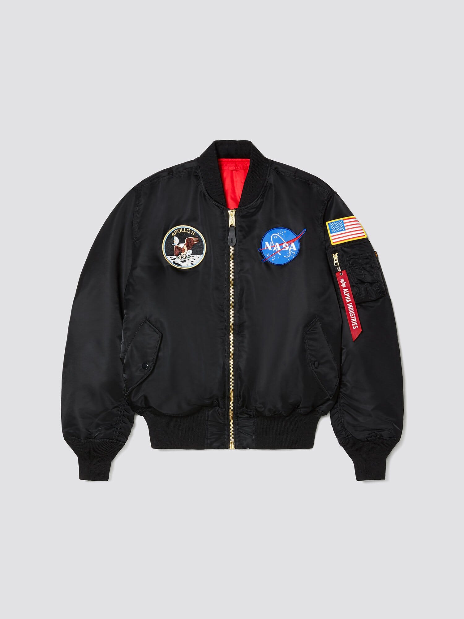 Alpha Industries Ma-1 Bomber Jacket in black with NASA and Apollo 11 patches, American flag sleeve patch, and red Remove Before Flight tag.