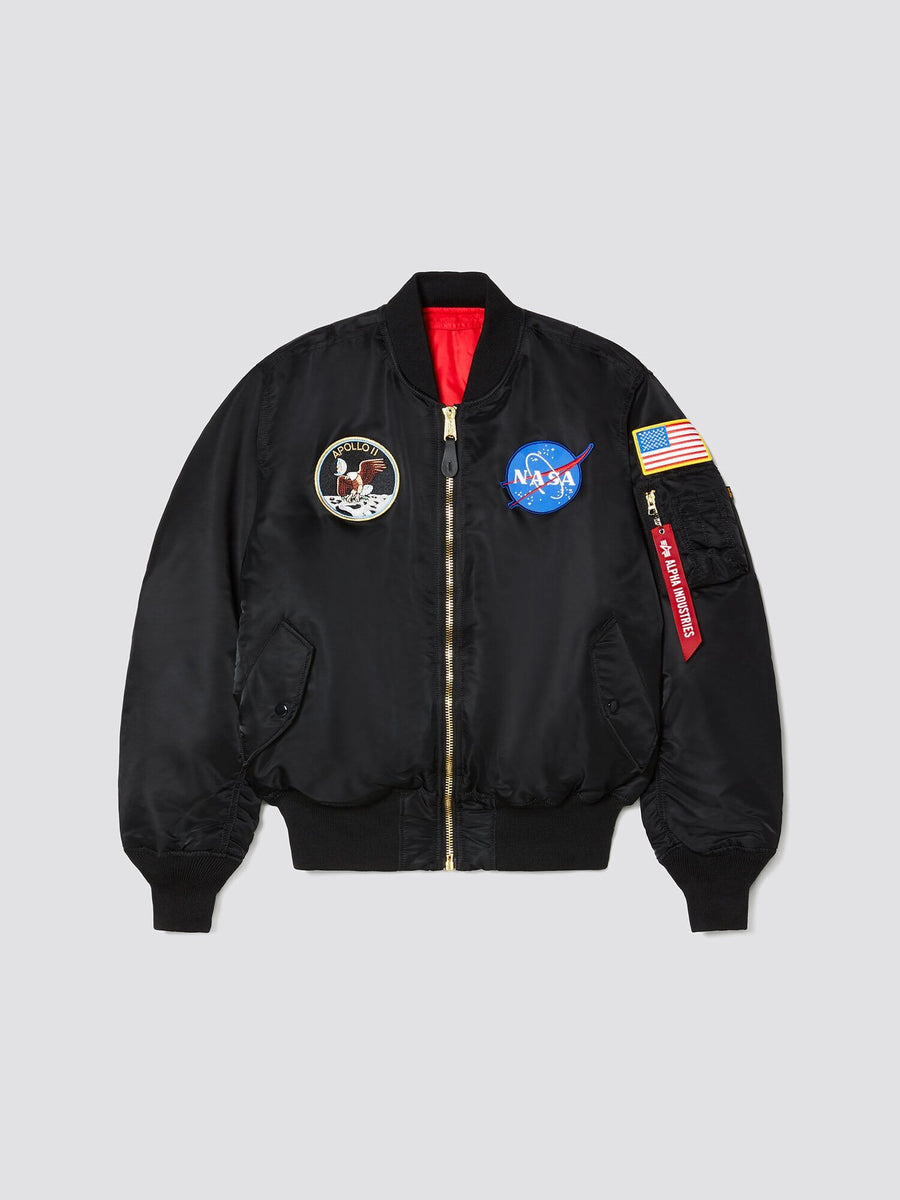 Alpha Industries Ma-1 Bomber Jacket in black with NASA and Apollo 11 patches, American flag sleeve patch, and red Remove Before Flight tag.
