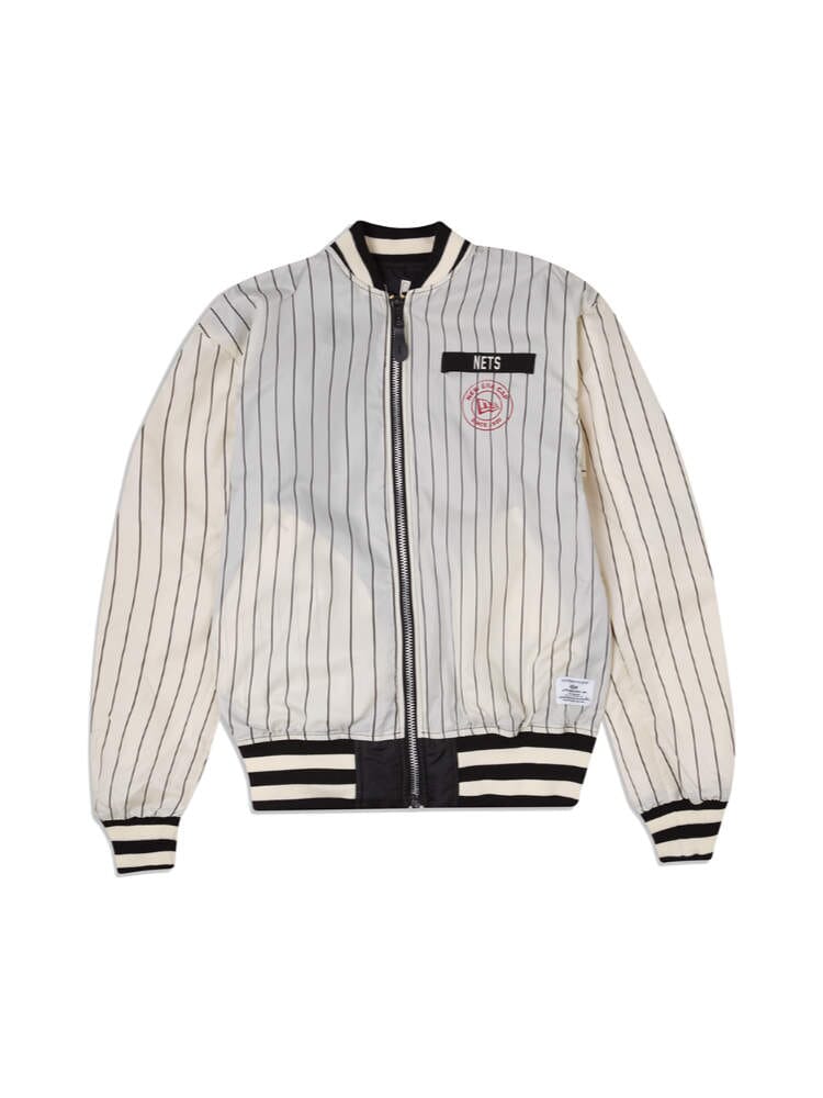 The Brooklyn Nets X Alpha X New Era L-2B Bomber Jacket by Alpha Industries and NE-NBA showcases a stylish white and black pinstripe design with various team patches, including a prominent Nets patch on the front and a circular logo. It features a zip closure along with ribbed cuffs and hem, ideal for fans eager to display their team pride in style.