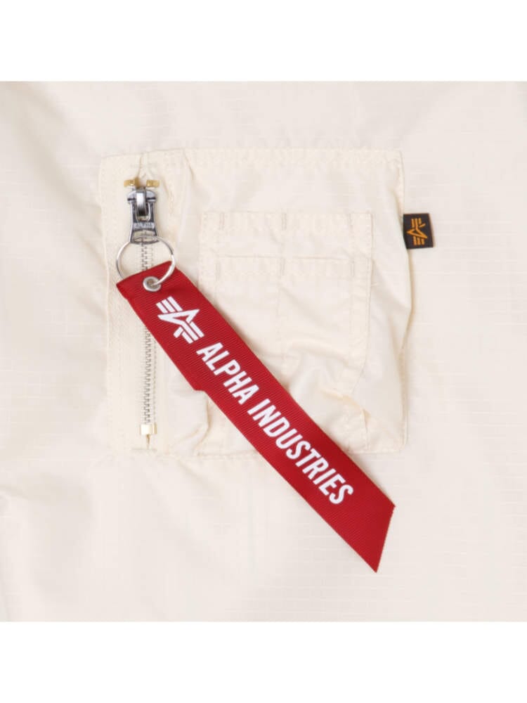 A red Alpha Industries tag is attached to a zipper on beige fabric with a small pocket, capturing the essence of the Chicago Bulls x Alpha x New Era L-2B Bomber Jacket.