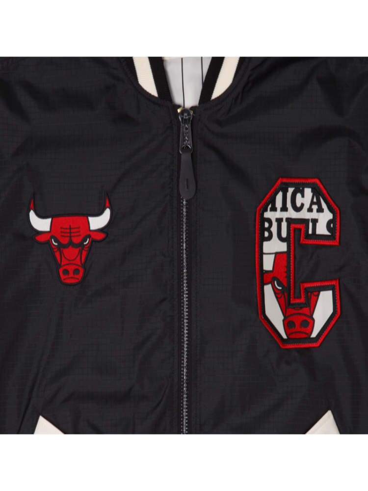 Close-up of a black Chicago Bulls X Alpha Industries X New Era L-2B Bomber Jacket showcasing a red bull logo alongside a stylized red and black C with the words Chicago Bulls partially visible, emphasizing its collaboration with Alpha Industries and NE-NBA.
