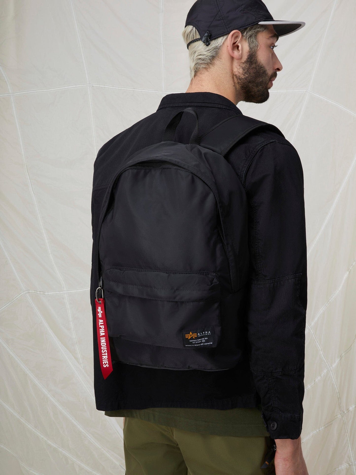 A man stands with his back to us, showcasing the ultra lightweight flight nylon Crew Backpack by Alpha Industries.