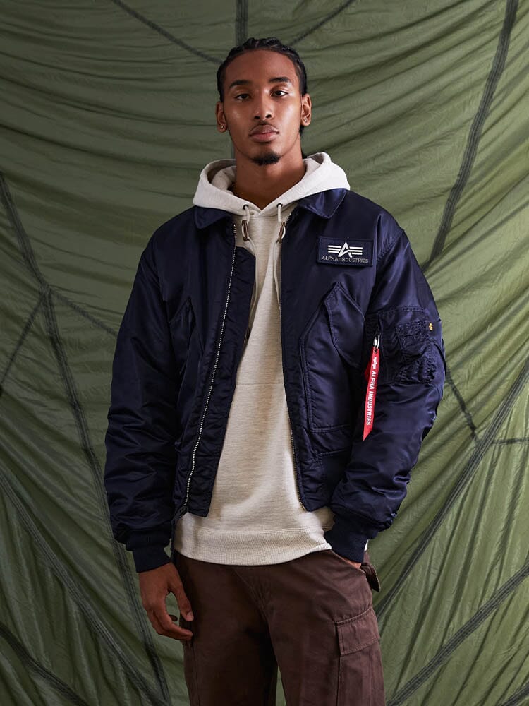 Alpha Industries Cwu 45/P Bomber Jacket in navy, worn over a light hoodie and brown pants.