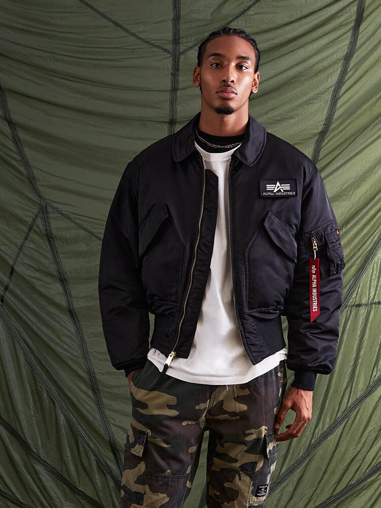 Alpha Industries Cwu 45/P Bomber Jacket in green with white shirt and camouflage pants.