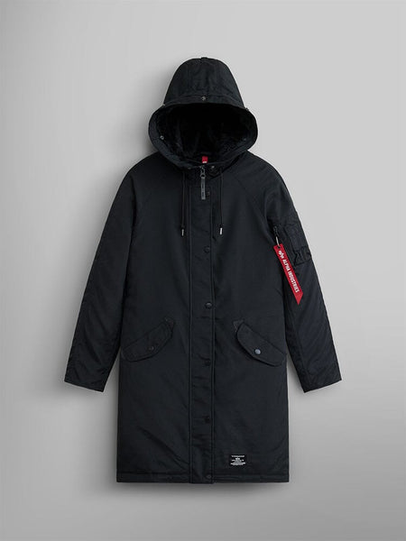 The Elyse Gen II Parka W by Alpha Industries is displayed. This black hooded parka comes with button and zip closures, a distinct red tag on the left sleeve, and features a faux fur-trimmed hood.