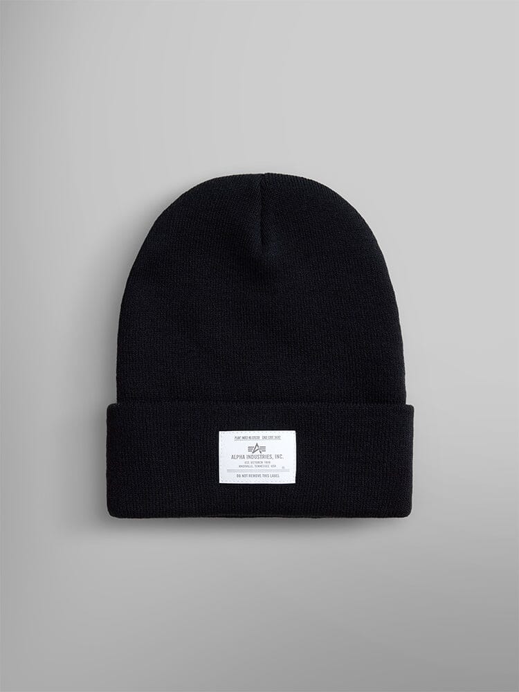 The Essential Beanie by Alpha Industries, Inc. is a black knit beanie with an Alpha paper label on the front, featuring a stylish folded brim.