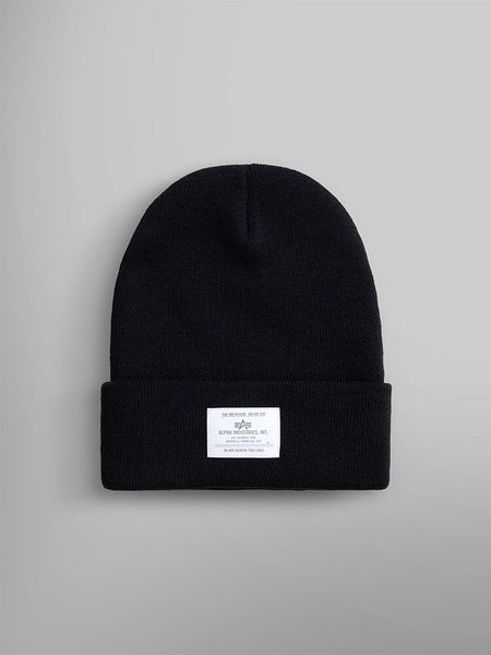 The Essential Beanie by Alpha Industries, Inc. is a black knit beanie with an Alpha paper label on the front, featuring a stylish folded brim.