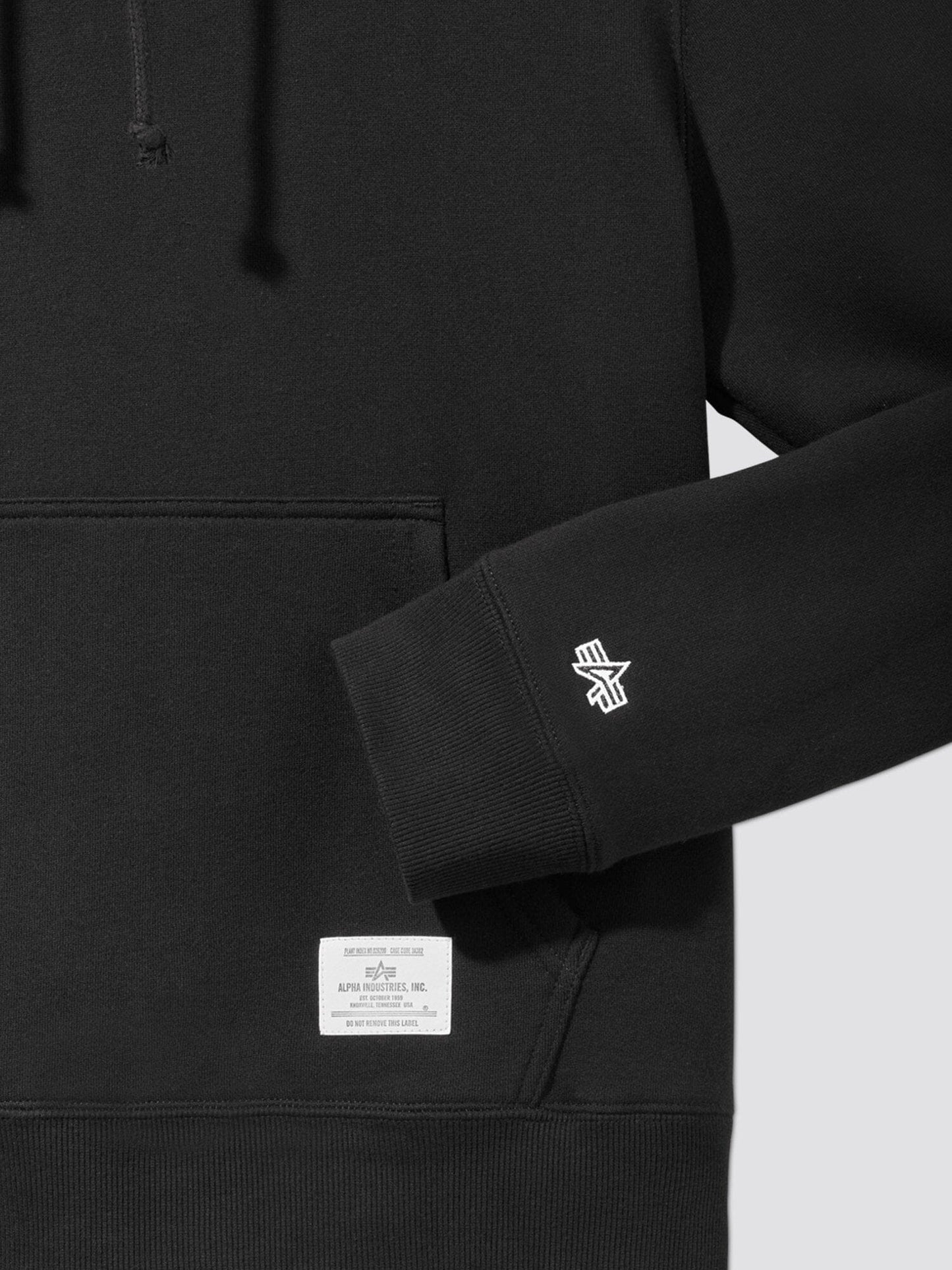 Close-up of the black Essential Hoodie, showcasing a front pocket, logo on the sleeve, and an Alpha Industries label above the pocket.