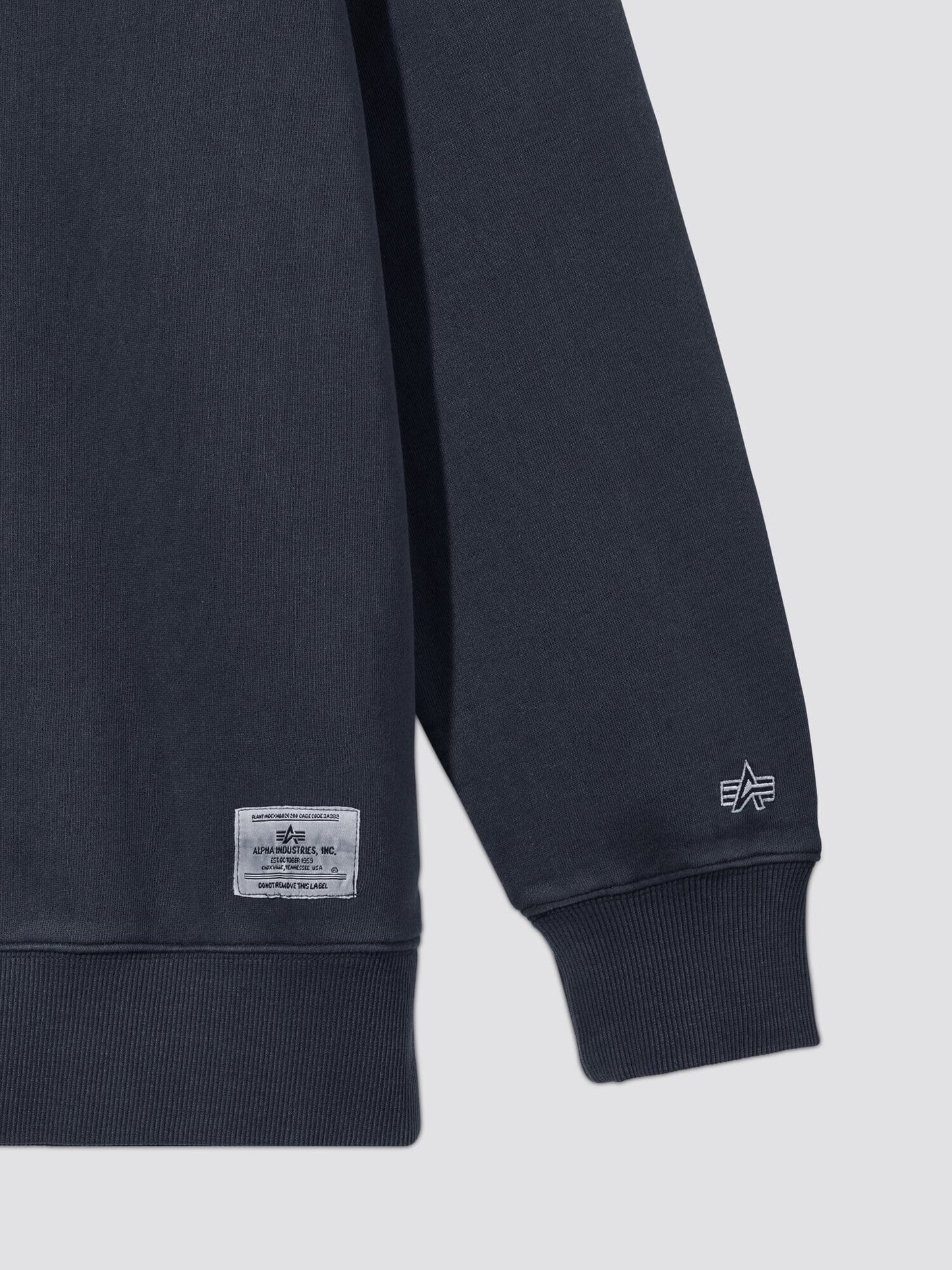 Essential Washed Crewneck by Alpha Industries, dark navy, ribbed cuff, small embroidered logo near hem, rectangular fabric label.