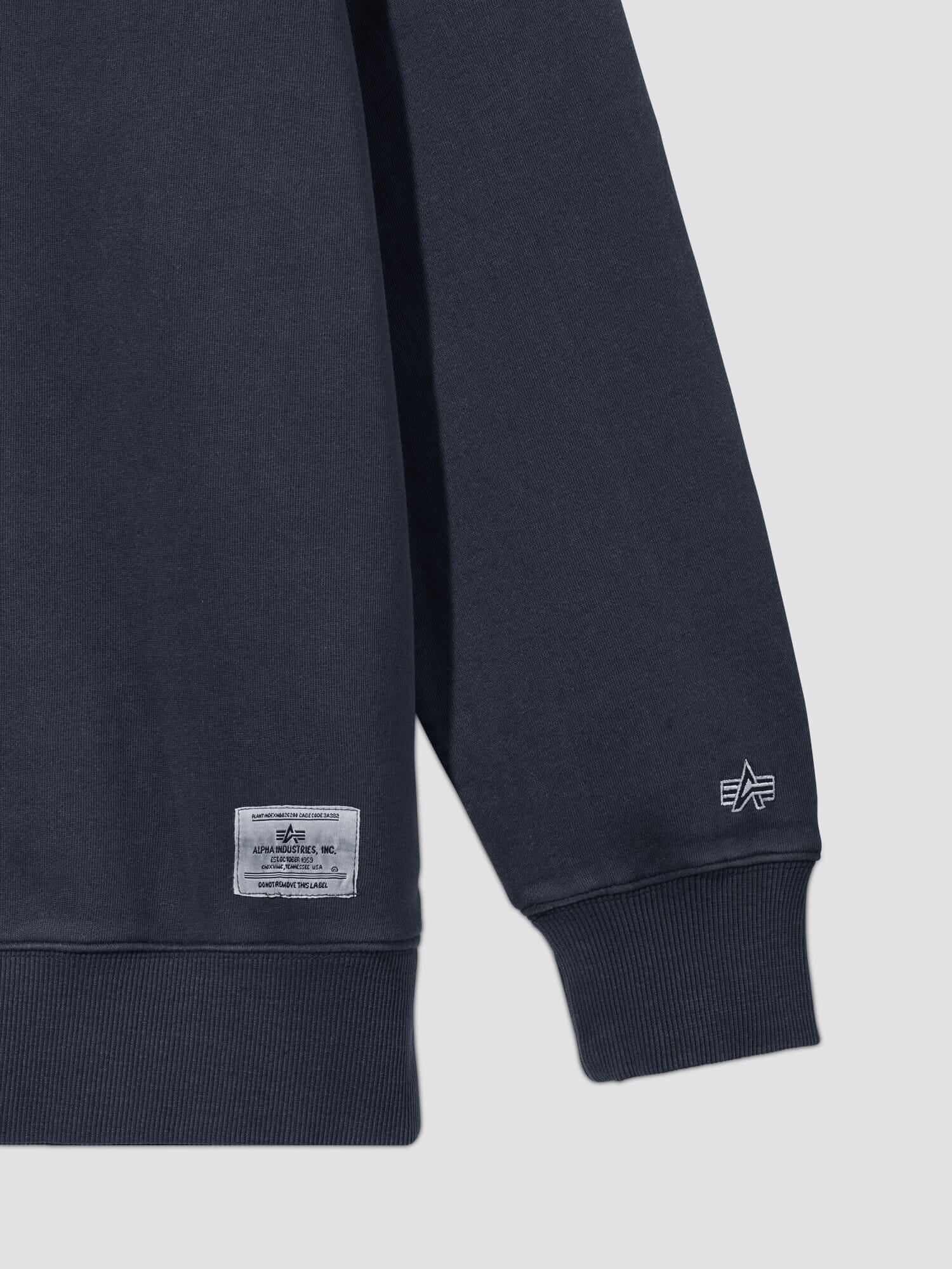 Essential Washed Crewneck by Alpha Industries, dark navy, ribbed cuff, small embroidered logo near hem, rectangular fabric label.