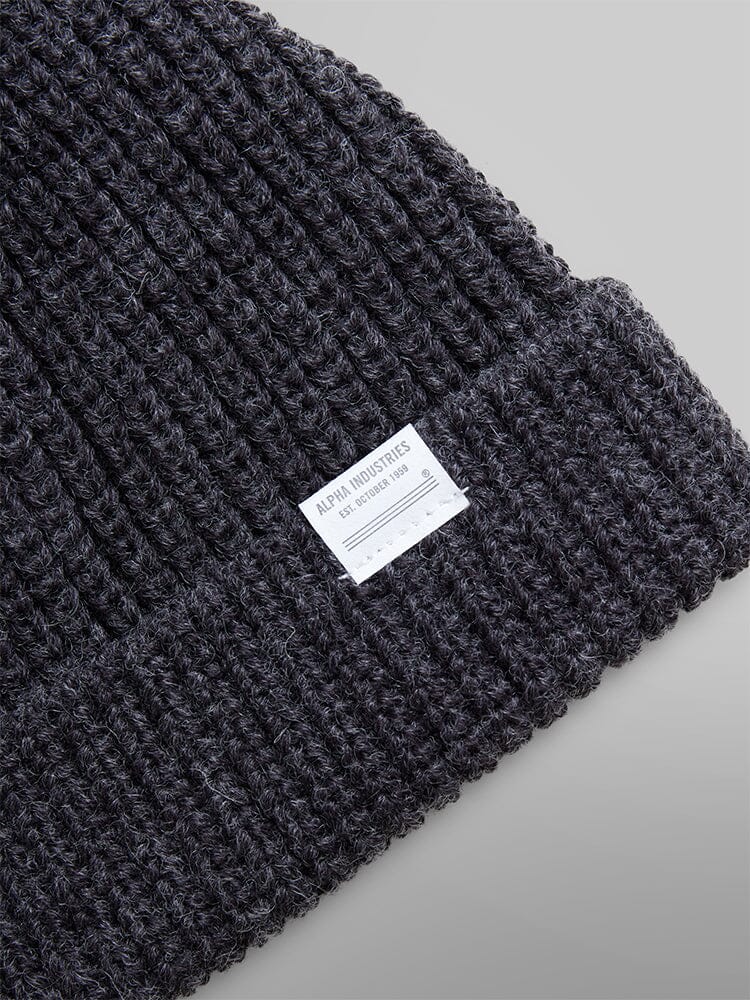 A close-up of the Essential Watch Cap by Alpha Industries in a gray wool-blend, featuring a white label with text, reminiscent of the classic style.